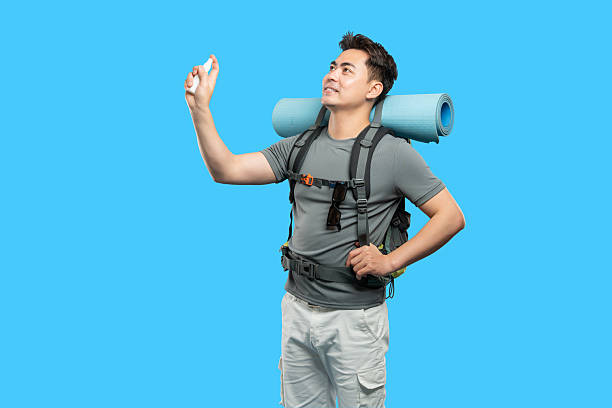 istock Man spraying sanitizer before outdoor adventure sporting backpack and rolled up mat against blue backdrop 2220743446