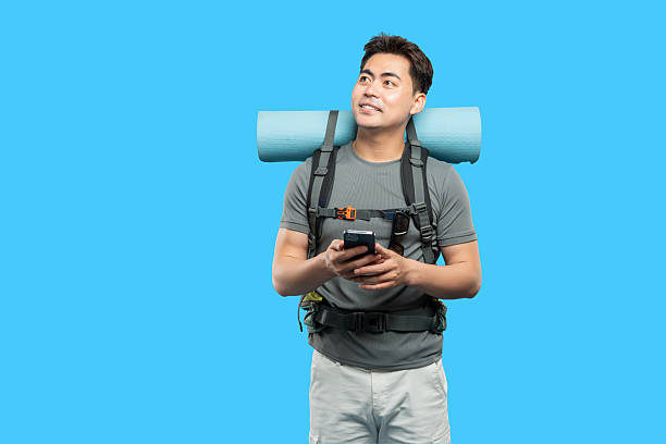 istock Adventurous man on a trip checks his phone with gear and backpack on a bright blue backdrop 2220746755