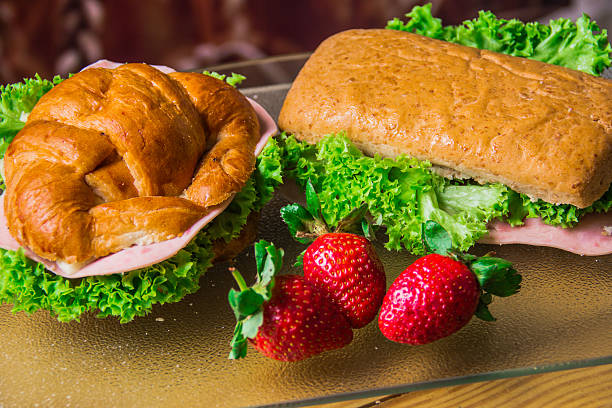 Two appetizing sandwiches filled with greens and ham, served alongside fresh strawberries, embodying a perfect blend of flavors for a wholesome meal or snack.
