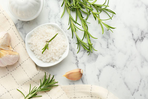 istock Sea salt, rosemary and garlic on white marble table, top view. Space for text 2220757723