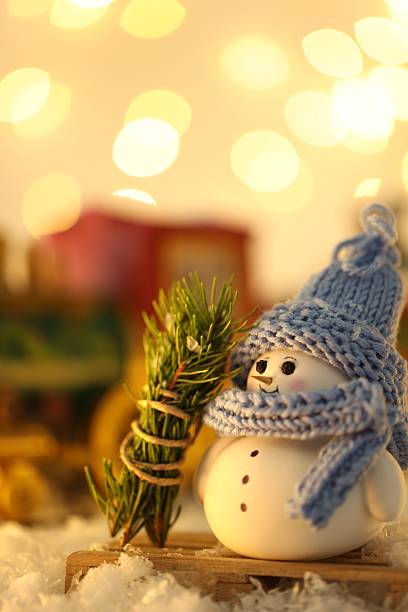 istock Cute decorative snowman and fir tree branches on artificial snow against blurred lights, closeup 2220758514