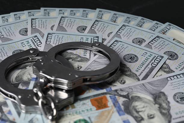 istock Corruption. Handcuffs and dollar banknotes on black table, closeup 2220759113