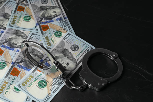 istock Corruption. Handcuffs and dollar banknotes on black table, closeup 2220759246