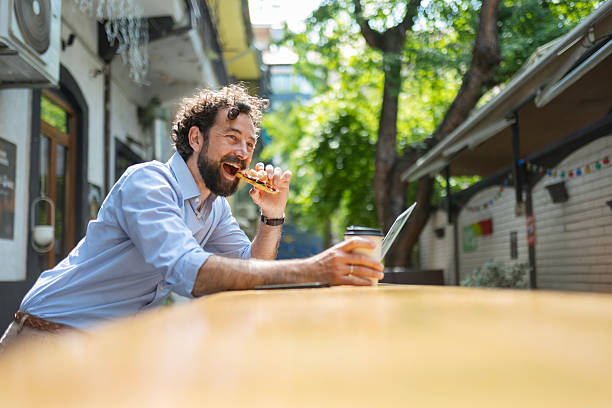istock Man Balancing Work and Relaxation Outdoors with Coffee Eating Sandwich 2220760972