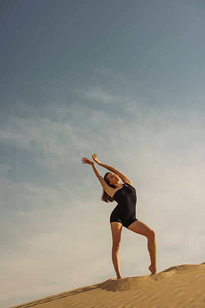 istock Woman performing elegant pose on sand dune under clear sky 2220762791