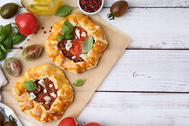 istock Tasty galettes with tomato, basil and cheese on white wooden table, flat lay. Space for text 2220765236