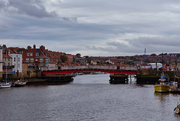 A red bridge spans a body of water under a cloudy sky in Whitby - North Yorkshire - Great Britain