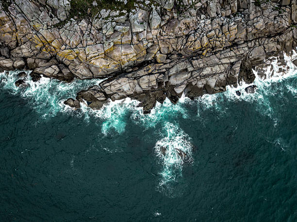 Aerial view directly above steep granite cliffs and rough seas