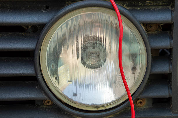 Details reveal a vehicle headlight with a clear lens, featuring a red wire connected to it, resting on a dark surface.