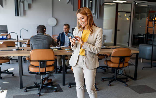 istock Businesswoman using smartphone in modern office with colleagues working 2220785621