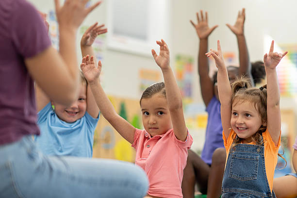 istock Preschool Children Enthusiastically Participating in a Classroom Activity with Raised Hands 2220789479