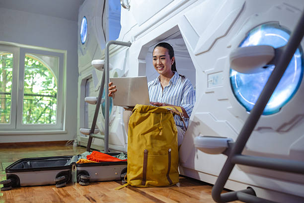 istock Traveler using a laptop in a capsule hotel with luggage and a window view 2220794873