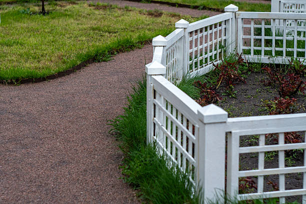 White fence with decorative lamps. Close-up view of a white picket fence with spherical decorative lamps on a blurred green background, creating a feeling of peace, suburbia