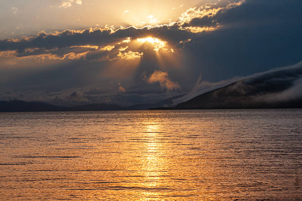 The sun's golden embrace kisses the horizon, casting a radiant farewell upon the tranquil sea, as hues of orange and pink dance upon the waves in a breathtaking seaside sunset.