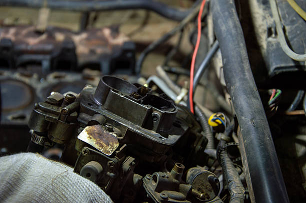 Mechanics work on a vehicle's engine, highlighting a carburetor and adjacent mechanical parts in a garage setting.