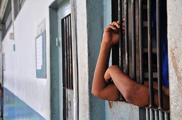 istock hands of a prisoner behind prison bars on black background 2220807611