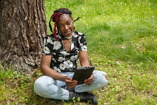 istock African American Student with Colorful Braids Using Digital Tablet in Park for Learning 2220813703