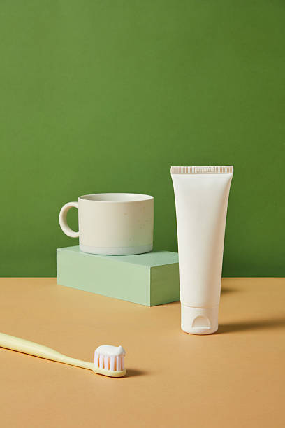 istock Toothpaste tube and ceramic mug placed on a yellow platform against a green backdrop, styled in clean minimalist aesthetic for modern bathroom product presentation. 2220825010