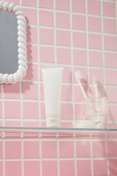 istock Vertical setup with cosmetic tube, mirror, and brushes in a pink tile bathroom. Soft lighting highlights the clean aesthetic and empty center space for product mockup. 2220825113