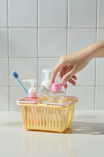 istock A hand reaches into a yellow plastic basket containing personal care items, placed in front of a white square tile wall. A bright, everyday hygiene scene with minimalist styling. 2220827786