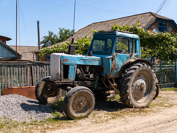 A blue tractor parked on a dirt road next to a fence.
