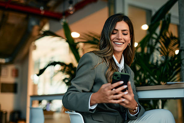 istock Businesswoman smiling while using mobile phone in modern office 2220840168
