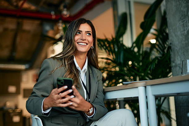 istock Young businesswoman smiling and looking away while using smartphone in office 2220840169