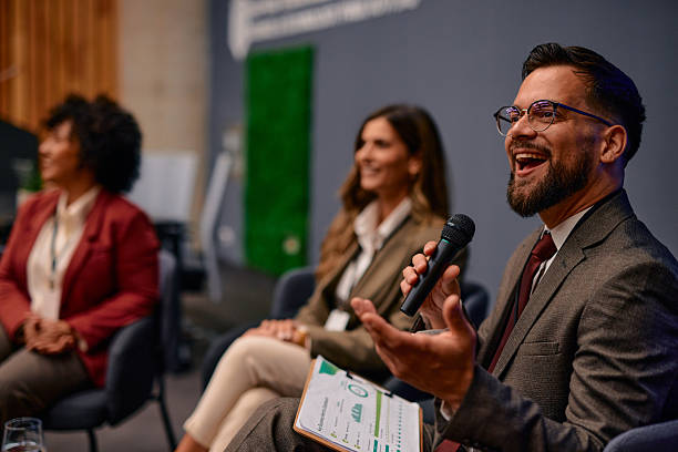 istock Businessman laughing while speaking into microphone at a conference 2220840301