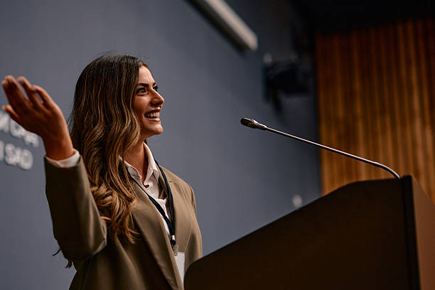 istock Businesswoman presenting at a conference, speaking on stage with microphone 2220841231