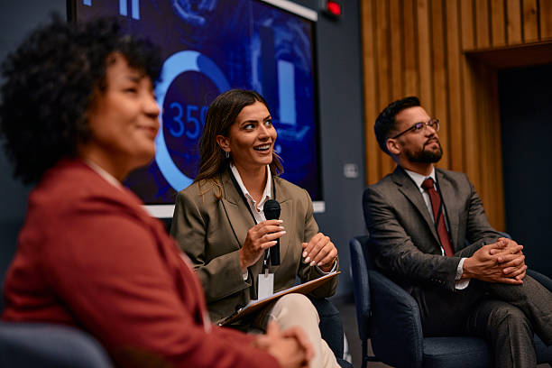 istock Businesswoman speaking at a conference using a microphone, sitting next to her colleagues 2220841349