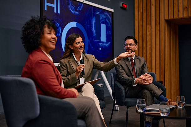 istock Businesswoman speaking at a conference using a microphone, sitting next to colleagues 2220841369