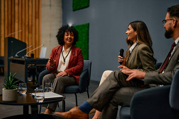 istock Businesswoman speaking at a conference using a microphone, sitting next to other speakers 2220841439