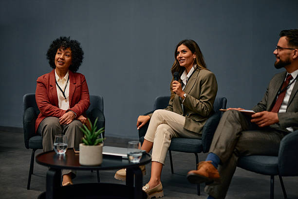 istock Businesswoman speaking at a conference using a microphone, sitting next to colleagues 2220841453