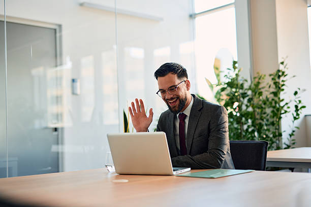 istock Businessman waving at laptop during video call in modern office 2220842003