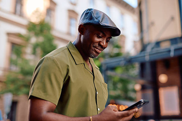 istock Stylish man wearing a flat cap is using his smartphone in the city center 2220844069