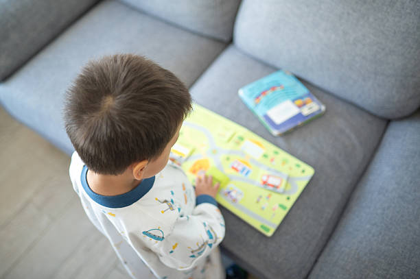 A 3 year old boy wearing pajamas plays with a book at home, showcasing a cozy and imaginative scene.