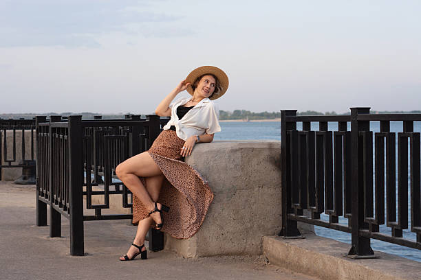 Smiling woman reclines on river wall in summer outfit