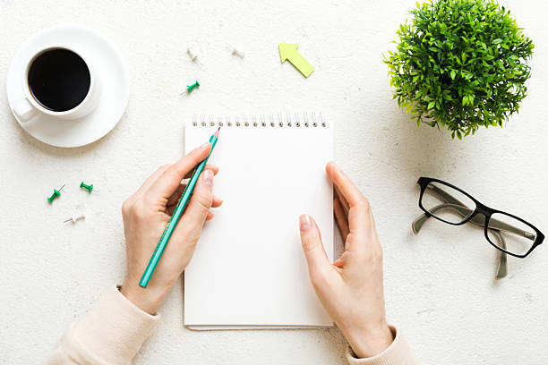 istock Woman hand with pencil writing on notebook and hold coffee cup. Woman working on office table with coffee 2220863784