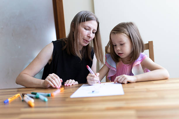 istock Babysitter helping little girl with homework, drawing with felt-tip pens 2220865574