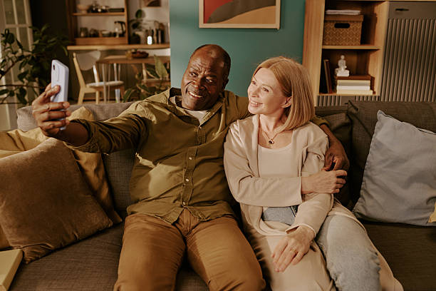 istock Senior Multiethnic Couple Sitting Together Taking Selfie Embracing on Sofa 2220867432