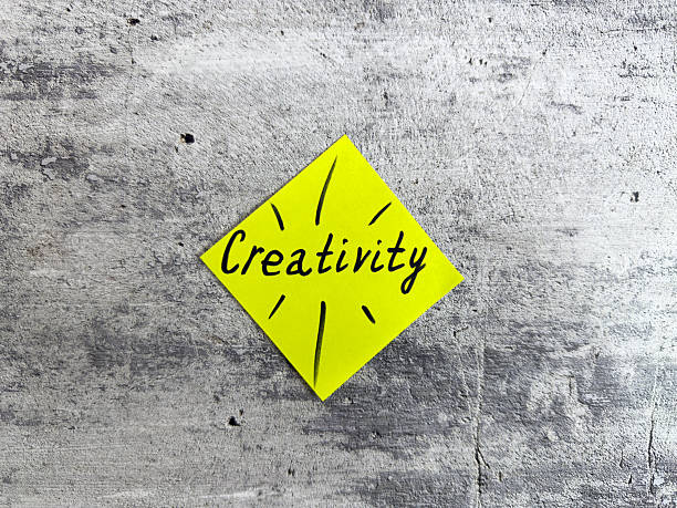 Vibrant yellow sticky note shaped as a diamond displaying the word Creativity and decorative elements on a textured grey background, representing the essence of innovative thinking and inspiration