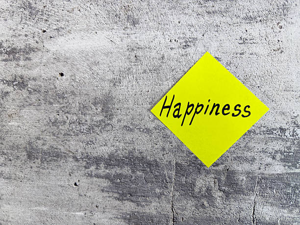 istock Bright yellow diamond-shaped sticky note with the word Happiness on a textured grey background, symbolizing joy and the importance of a positive outlook in daily life 2220867999