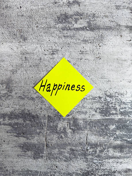 istock Vertical photograph showcasing a bright yellow diamond-shaped sticky note with the word Happiness against a textured grey background, symbolizing joy and positivity in daily life 2220868005