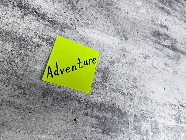istock Bright yellow sticky note displaying word Adventure placed on textured grey background, representing themes of exploration, creativity, and the excitement of new journeys 2220868017