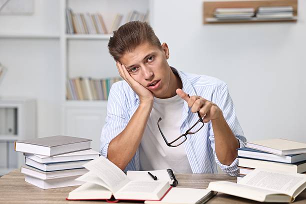 istock Tired student before exam at table among books indoors 2220872420