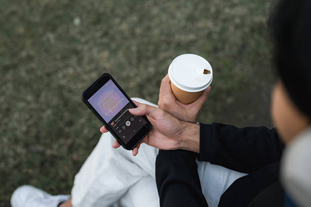 istock Young man relaxing by the sidewalk, scrolling through his smartphone while music plays through his headphones 2220874835