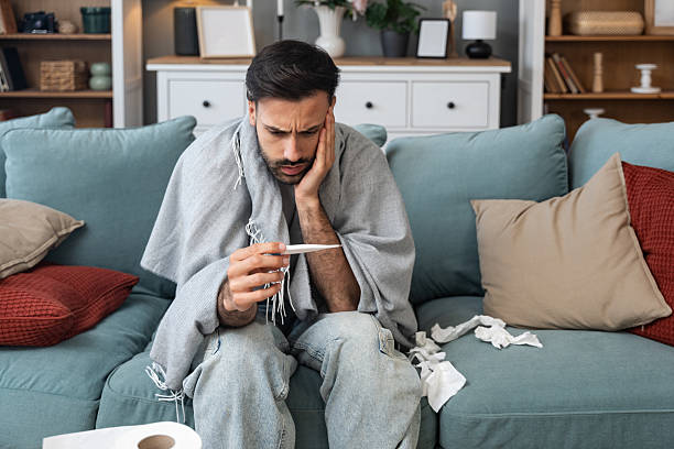 istock Ill man lying wrapped in blanket and checking temperature at home, experiencing high fever, weakness, and physical discomfort during cold infection and trying to recover from viral flu symptoms 2220875310