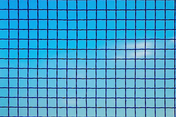 A vibrant blue wire mesh fence forms a perfect grid pattern against a clear, bright blue sky. This abstract background suggests themes of security, boundaries, or a clean, modern aesthetic