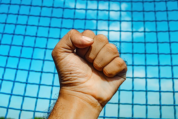 A powerful human fist is raised against a vibrant blue mesh net and clear sky, symbolizing strength, determination, or breaking through limitations. Ideal for themes of freedom and resilience