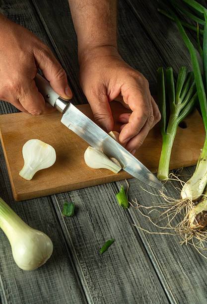 istock Hands skillfully chop scallions on a cutting board, surrounded by fresh vegetables. The bright green of the scallions contrasts with the wooden surface, creating a vibrant kitchen atmosphere 2220880033